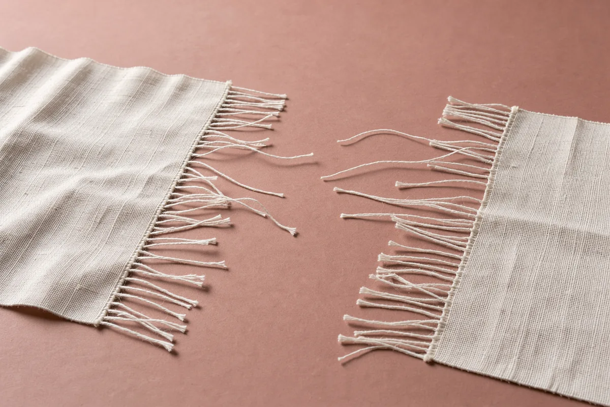 Two open edges of pale woven cloth approach each other across a rose-clay surface.